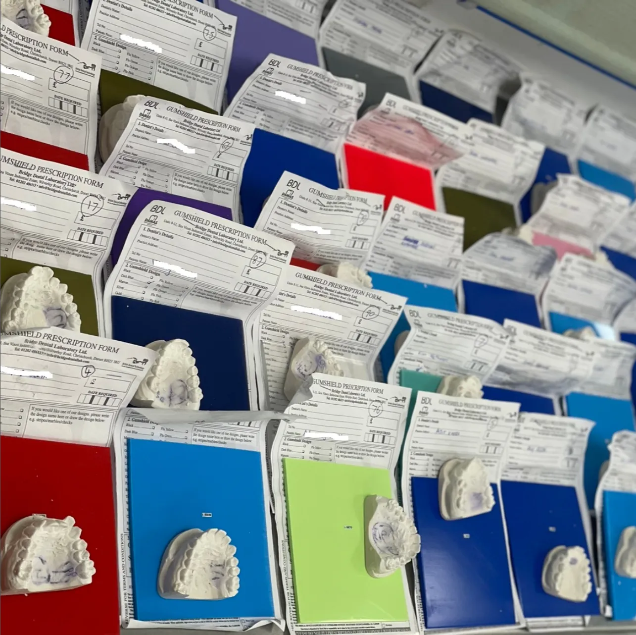 A large squad order of custom gumshields laid out on the bench beside their prescription forms and dental models
