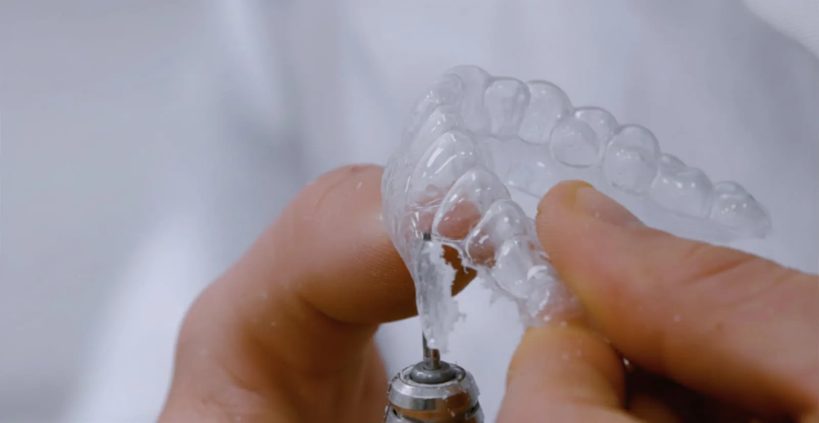A Bridge Dental technician trimming and finishing a clear whitening tray with a rotary handpiece